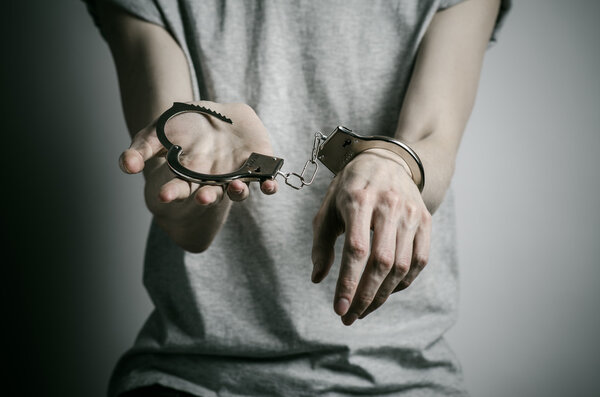 Prison and convicted topic: man with handcuffs on his hands in a gray T-shirt on a gray background in the studio, put handcuffs on rapist