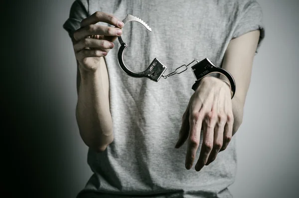 Prison and convicted topic: man with handcuffs on his hands in a gray T-shirt on a gray background in the studio, put handcuffs on rapist — Stock Photo, Image