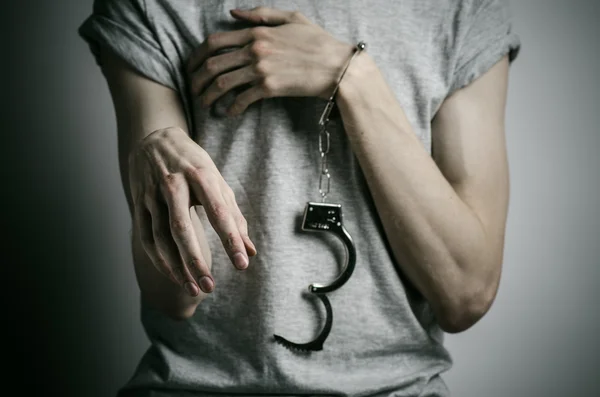 Fängelse och dömda ämne: mannen med handfängsel på händerna i en grå T-shirt på en grå bakgrund i studion, sätta handfängsel på våldtäktsmannen — Stockfoto