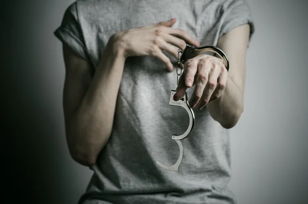 Тюрьма и осужденная тема: человек с наручниками на руках в серой футболке на сером фоне в студии, надел наручники на насильника — стоковое фото
