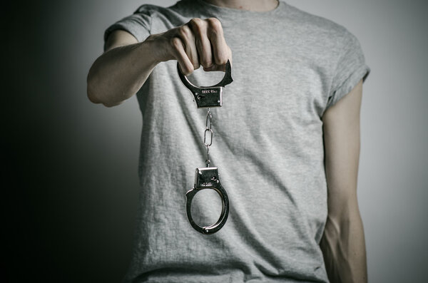 Prison and convicted topic: man with handcuffs on his hands in a gray T-shirt on a gray background in the studio, put handcuffs on rapist
