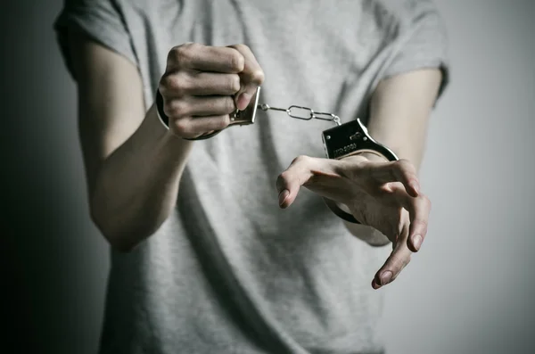 Fängelse och dömda ämne: mannen med handfängsel på händerna i en grå T-shirt på en grå bakgrund i studion, sätta handfängsel på våldtäktsmannen — Stockfoto