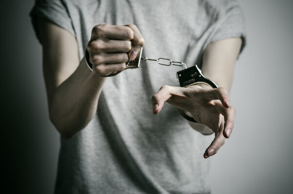 Prison and convicted topic: man with handcuffs on his hands in a gray T-shirt on a gray background in the studio, put handcuffs on rapist