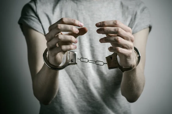 Gevangenis en veroordeelde onderwerp: man met handboeien op zijn handen in een grijs T-shirt op een grijze achtergrond in de studio, handboeien zetten verkrachter — Stockfoto