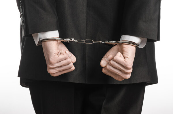 Corruption and bribery theme: businessman in a black suit with handcuffs on his hands on a white background in studio isolated