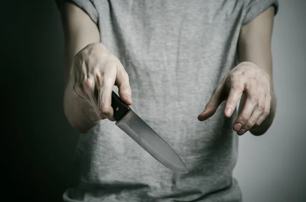 Tema Pembunuhan dan Halloween: Seorang pria memegang pisau dengan latar belakang abu-abu — Stok Foto