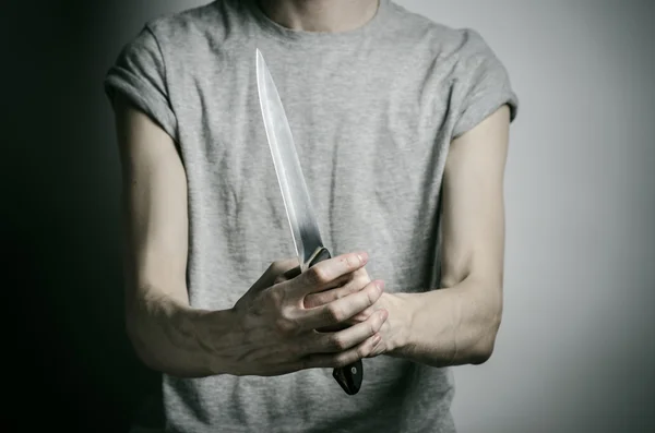 El asesinato y el tema de Halloween: un hombre sosteniendo un cuchillo sobre un fondo gris — Foto de Stock