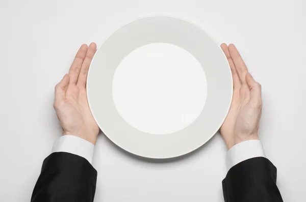 Pranzo di lavoro e cibo sano tema: la mano dell'uomo in un abito nero che tiene un piatto bianco vuoto e mostra il gesto delle dita su uno sfondo bianco isolato in studio vista dall'alto — Foto Stock