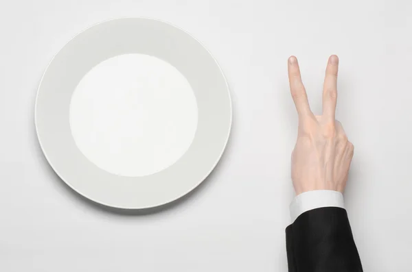 Business lunch and healthy food theme: man's hand in a black suit holding a white empty plate and shows finger gesture on an isolated white background in studio top view — Stock Photo, Image