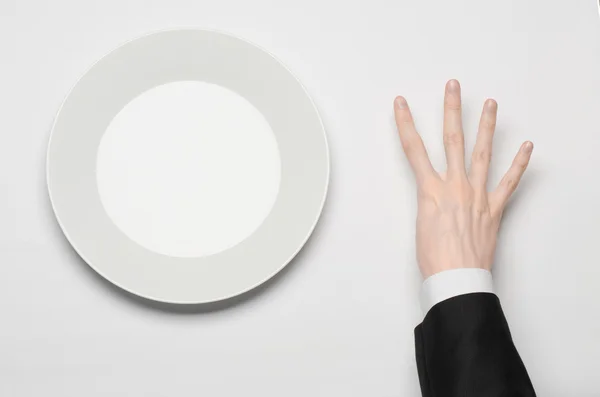 Pracovní oběd a zdravé potraviny téma: člověk ruku v černém obleku drží bílý prázdný talíř a ukazuje prstem gesto na izolované bílém pozadí v pohledu shora studio — Stock fotografie