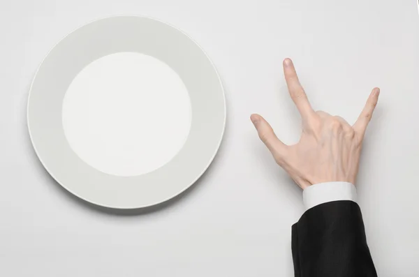 Pranzo di lavoro e cibo sano tema: la mano dell'uomo in un abito nero che tiene un piatto bianco vuoto e mostra il gesto delle dita su uno sfondo bianco isolato in studio vista dall'alto — Foto Stock