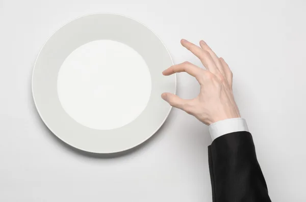 Pranzo di lavoro e cibo sano tema: la mano dell'uomo in un abito nero che tiene un piatto bianco vuoto e mostra il gesto delle dita su uno sfondo bianco isolato in studio vista dall'alto — Foto Stock