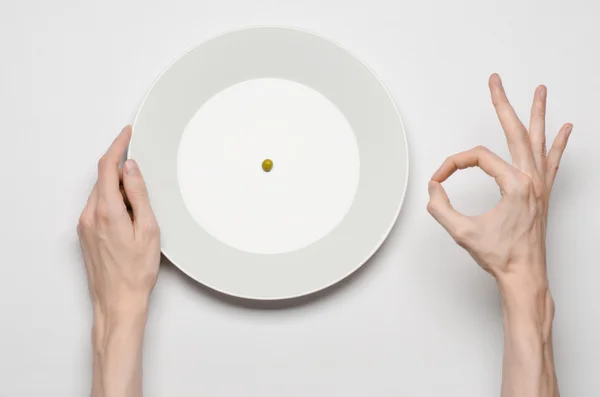 Тема здорового питания: руки, держащие нож и вилку на тарелке с зеленым горошком на белом столе вид сверху — стоковое фото