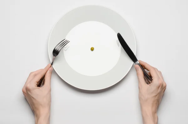 Tema de comida saludable: manos sosteniendo cuchillo y tenedor en un plato con guisantes verdes en una mesa blanca vista superior —  Fotos de Stock