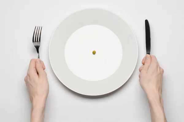 Тема здорового питания: руки, держащие нож и вилку на тарелке с зеленым горошком на белом столе вид сверху — стоковое фото