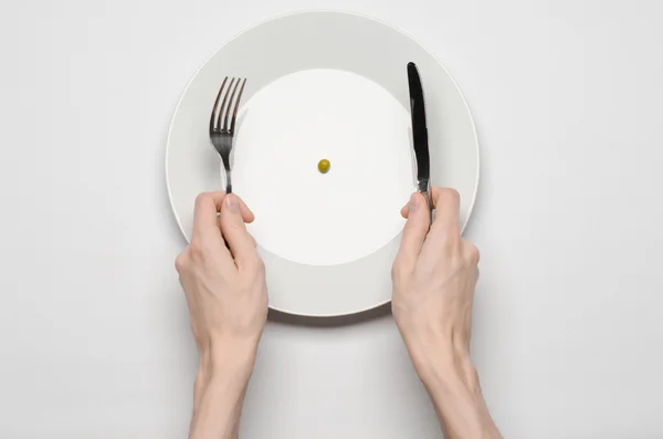 Tema del cibo sano: mani che tengono coltello e forchetta su un piatto con piselli verdi su un tavolo bianco vista dall'alto — Foto Stock