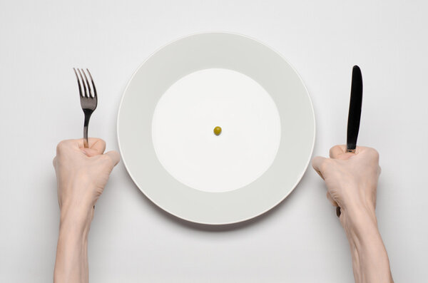 Тема здорового питания: руки, держащие нож и вилку на тарелке с зеленым горошком на белом столе вид сверху
