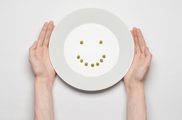 Healthy food theme: hands holding a plate of green peas on a white table top view