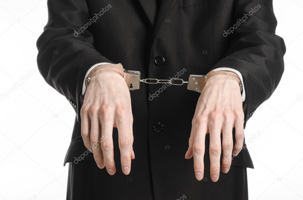 Corruption and bribery theme: businessman in a black suit with handcuffs on his hands on a white background in studio isolated