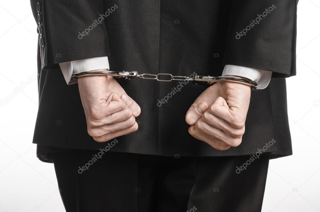 Corruption and bribery theme: businessman in a black suit with handcuffs on his hands on a white background in studio isolated