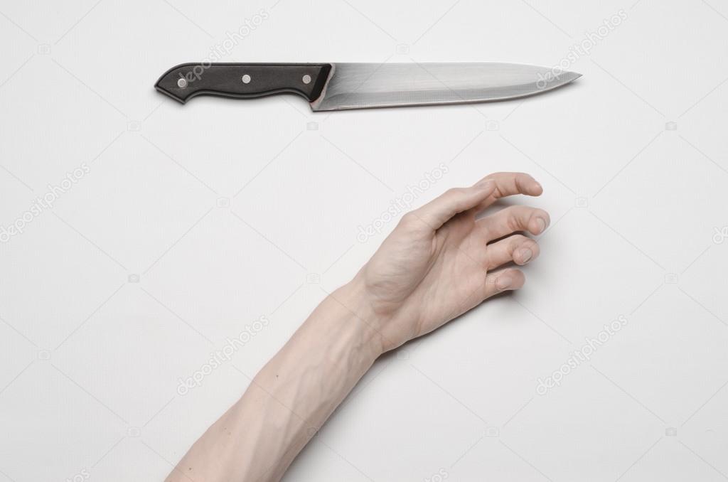 Murder and Halloween theme: A man's hand reaching for a knife, a human hand holding a knife isolated on a gray background in studio from above