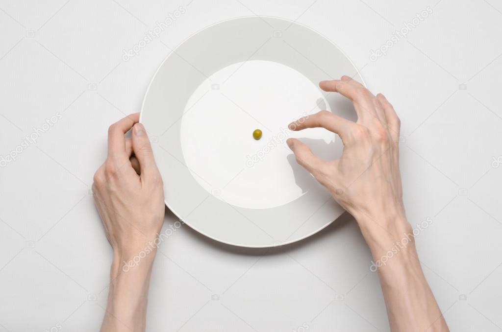 Healthy food theme: hands holding knife and fork on a plate with green peas on a white table top view