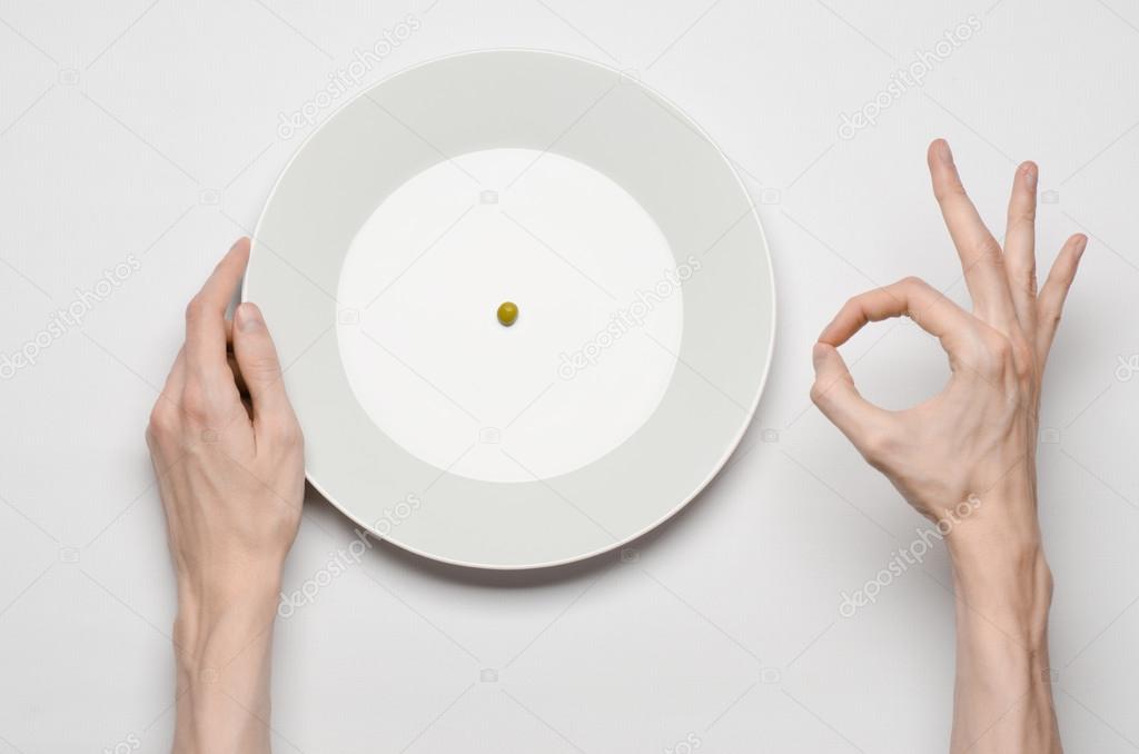 Healthy food theme: hands holding knife and fork on a plate with green peas on a white table top view