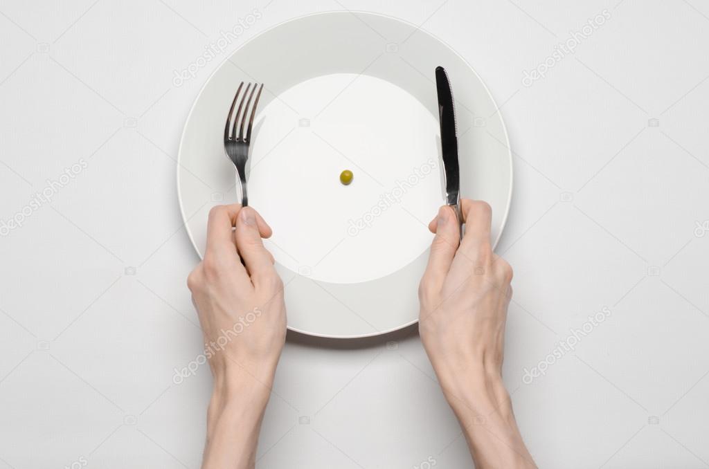 Healthy food theme: hands holding knife and fork on a plate with green peas on a white table top view