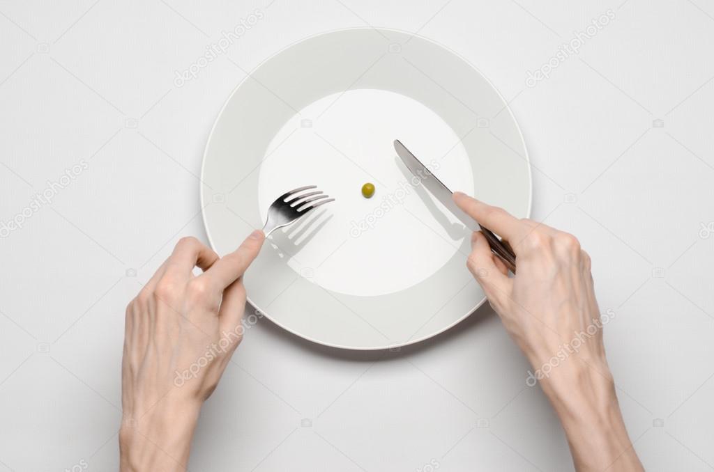 Healthy food theme: hands holding knife and fork on a plate with green peas on a white table top view