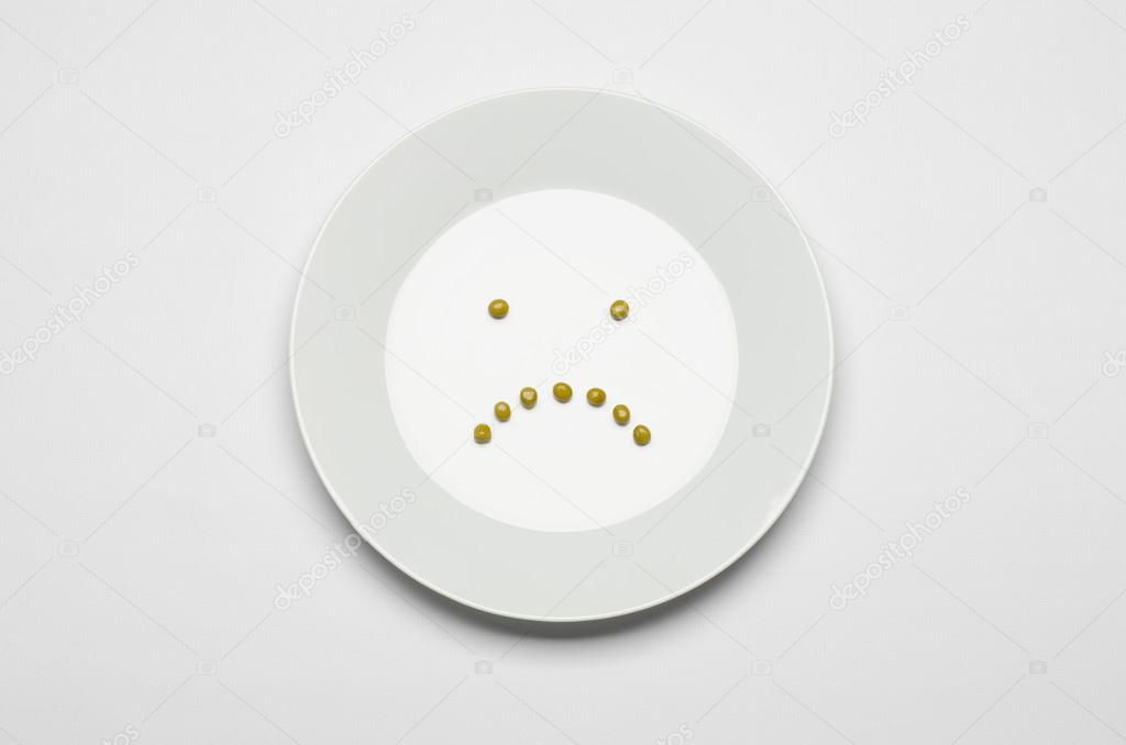 Healthy eating topic: green peas lying on a white plate on a white table in the studio, a sad smile top view