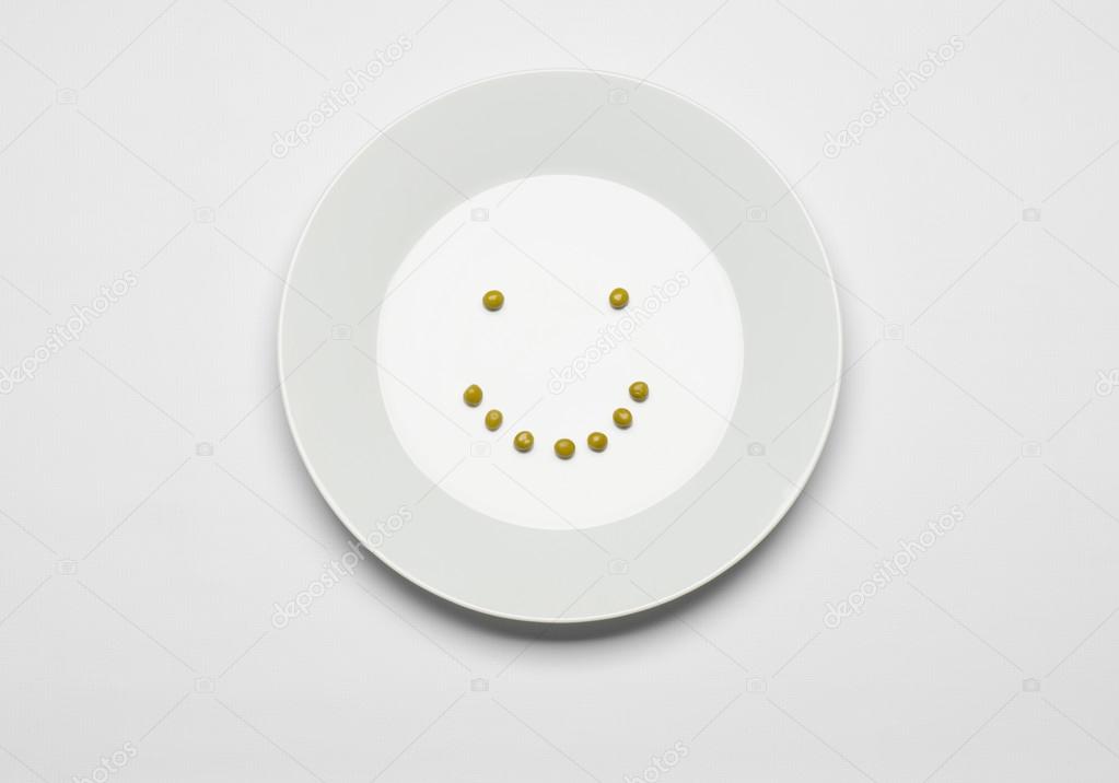Healthy eating topic: green peas lying on a white plate on a white table in the studio, cheerful smile top view