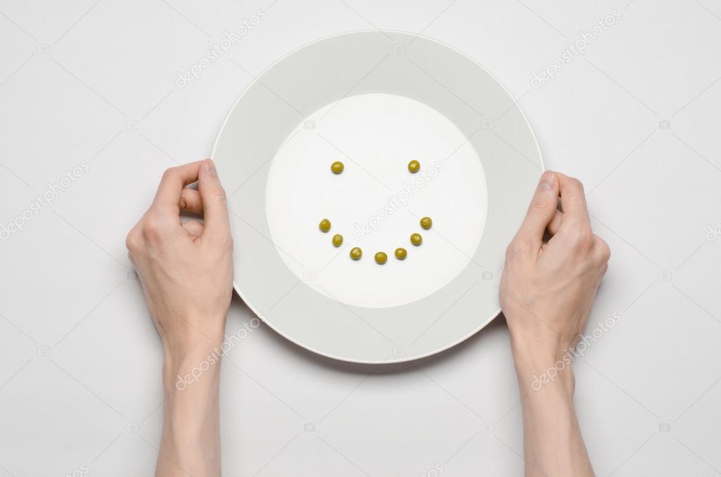 Healthy food theme: hands holding a plate of green peas on a white table top view