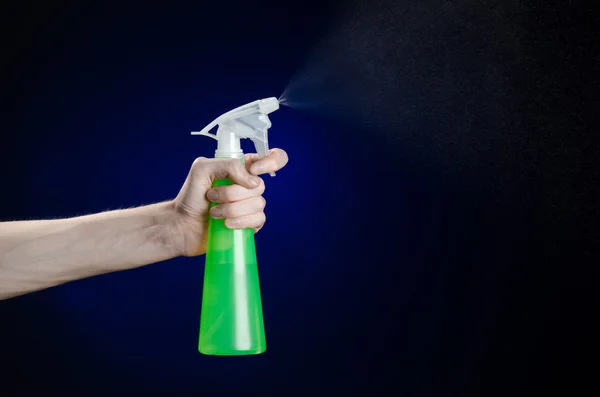 Cleaning the house and cleaner theme: man's hand holding a green spray bottle for cleaning on a dark blue background — Stock Photo, Image