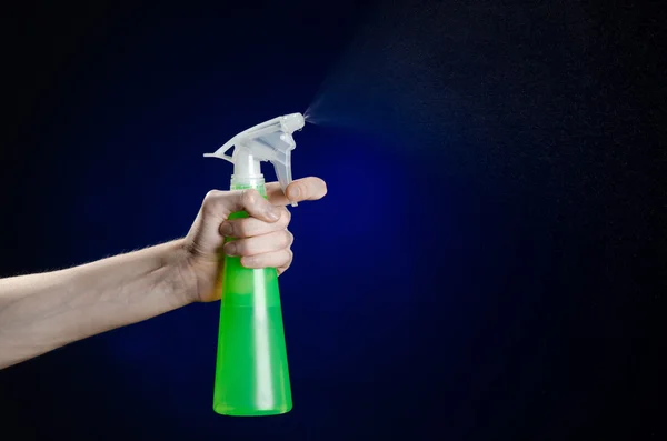 Limpieza de la casa y el tema más limpio: la mano del hombre sosteniendo una botella de spray verde para limpiar sobre un fondo azul oscuro — Foto de Stock