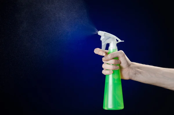 Limpieza de la casa y el tema más limpio: la mano del hombre sosteniendo una botella de spray verde para limpiar sobre un fondo azul oscuro — Foto de Stock