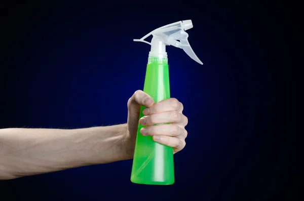 Membersihkan rumah dan tema yang lebih bersih: tangan manusia memegang botol semprotan hijau untuk membersihkan latar belakang biru tua — Stok Foto