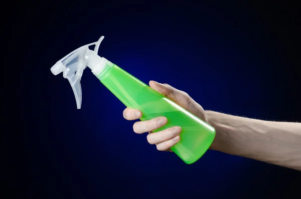 清洁的房子和更清洁的主题: 人的手拿着绿色喷雾瓶清洗上的深蓝色背景 — 图库照片
