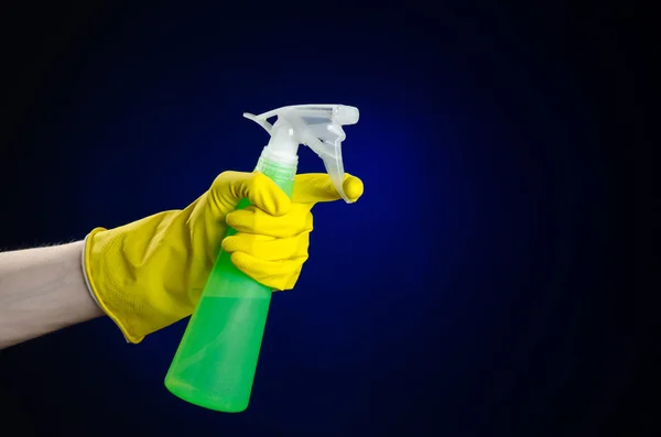 Limpieza de la casa y el tema más limpio: la mano del hombre en un guante amarillo con una botella de spray verde para limpiar sobre un fondo azul oscuro — Foto de Stock