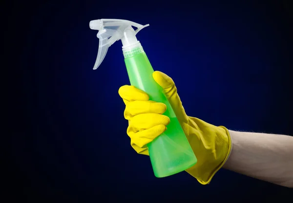 Pulizia della casa e tema più pulito: mano dell'uomo in un guanto giallo che tiene una bottiglia di spray verde per la pulizia su uno sfondo blu scuro — Foto Stock