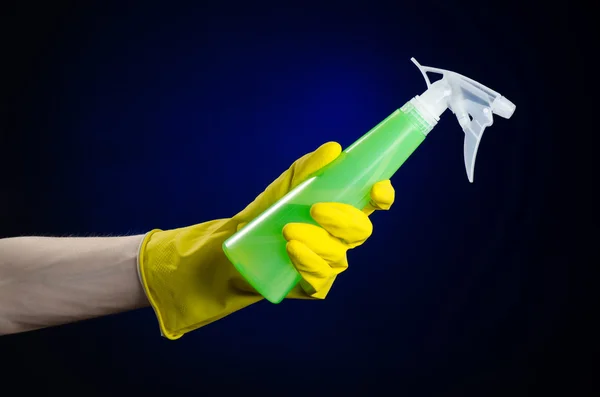 Limpieza de la casa y el tema más limpio: la mano del hombre en un guante amarillo con una botella de spray verde para limpiar sobre un fondo azul oscuro — Foto de Stock