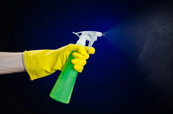 Limpieza de la casa y el tema más limpio: la mano del hombre en un guante amarillo con una botella de spray verde para limpiar sobre un fondo azul oscuro — Foto de Stock