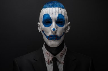 Terrible clown and Halloween theme: Crazy blue clown in black suit isolated on a dark background in the studio