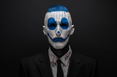 Terrible clown and Halloween theme: Crazy blue clown in black suit isolated on a dark background in the studio