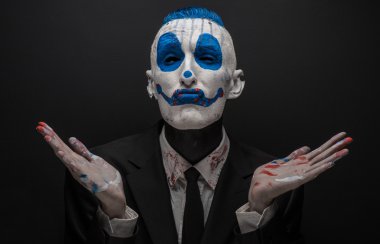 Terrible clown and Halloween theme: Crazy blue clown in black suit isolated on a dark background in the studio