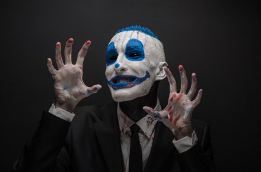 Terrible clown and Halloween theme: Crazy blue clown in black suit isolated on a dark background in the studio
