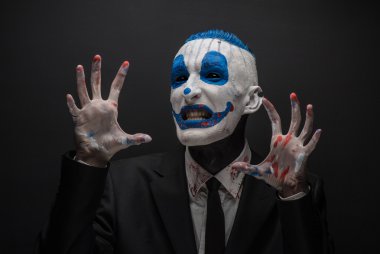 Terrible clown and Halloween theme: Crazy blue clown in black suit isolated on a dark background in the studio