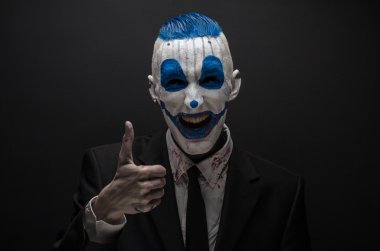 Terrible clown and Halloween theme: Crazy blue clown in black suit isolated on a dark background in the studio