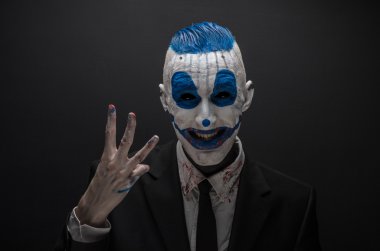 Terrible clown and Halloween theme: Crazy blue clown in black suit isolated on a dark background in the studio