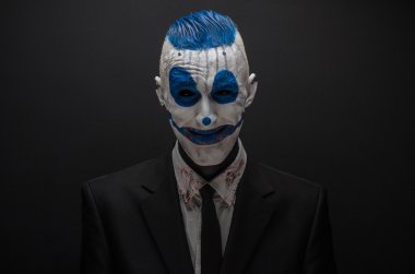 Terrible clown and Halloween theme: Crazy blue clown in black suit isolated on a dark background in the studio