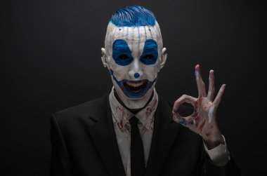 Terrible clown and Halloween theme: Crazy blue clown in black suit isolated on a dark background in the studio